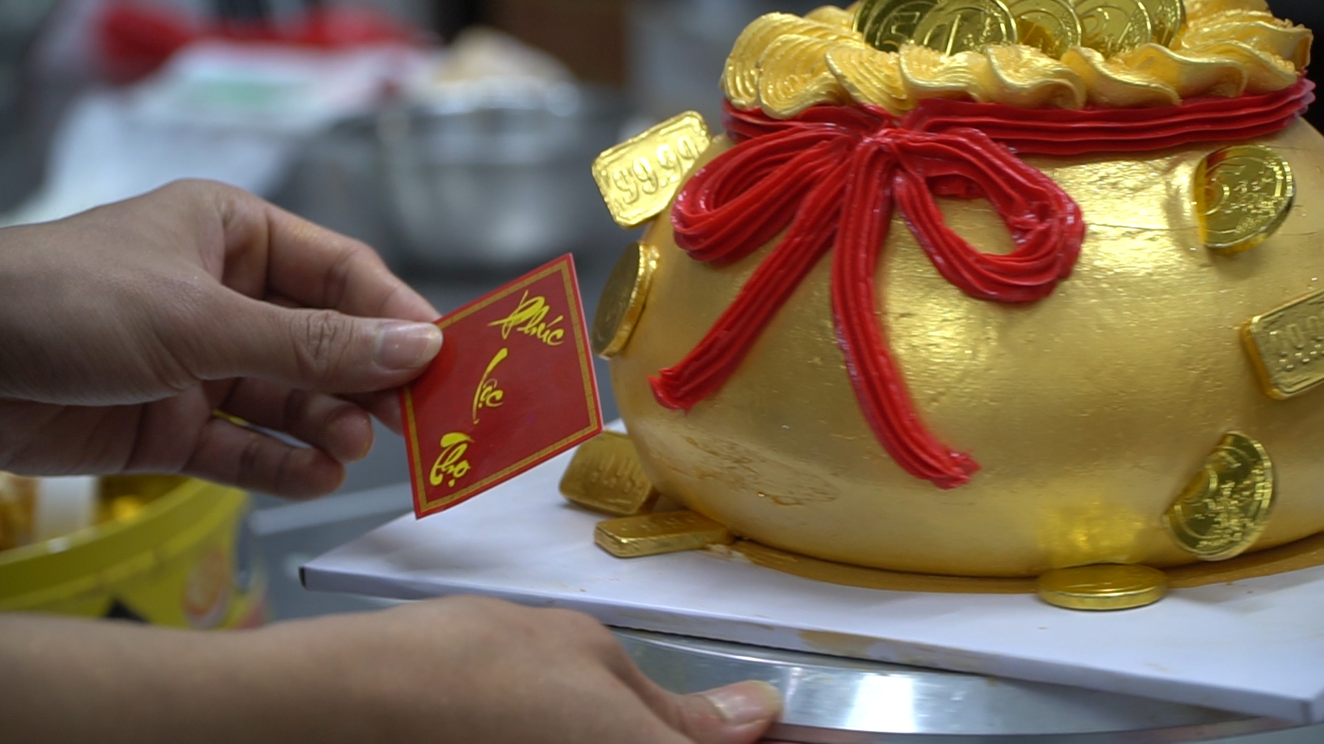 Bánh kem hình hũ vàng được “gọt giũa” để bánh có hình tròn, bên ngoài bọc thêm lớp kem tươi và được trang trí bằng những họa tiết đồng tiền vàng lấp lánh