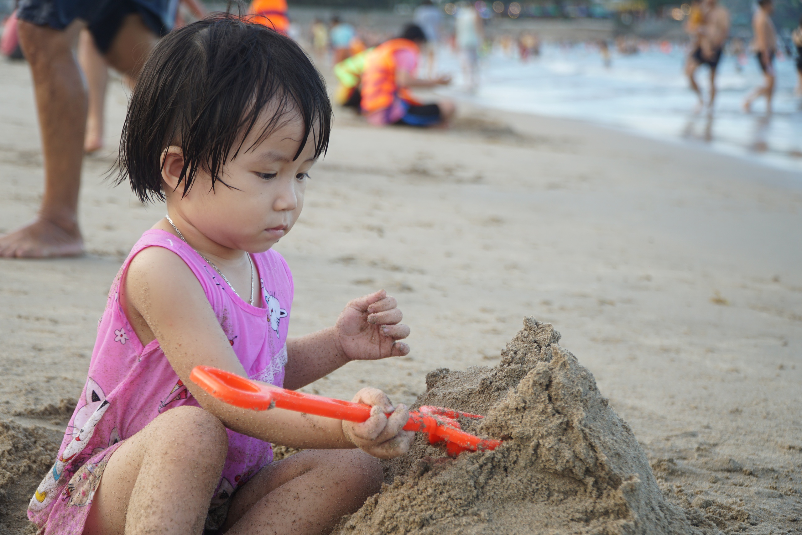 Một em nhỏ tranh thủ ngồi chơi đùa với cát trên bờ biển Nha Trang