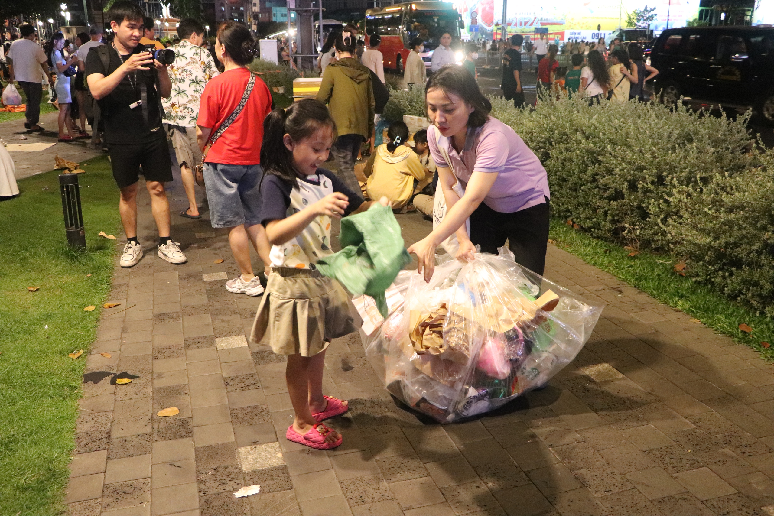 Người phụ nữ cùng con gái thu gom rác vào túi, vận chuyển cho công nhân vệ sinh môi trường xử lý