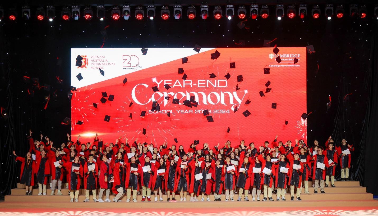 A group of people standing in front of a red banner with graduation caps  Description automatically generated