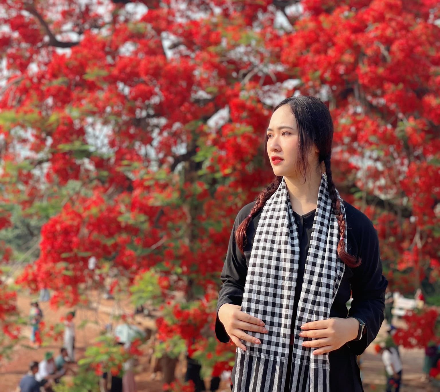 Trần Linh Ngọc trong trang phục áo bà ba, khăn rằn chụp hình với hoa phượng