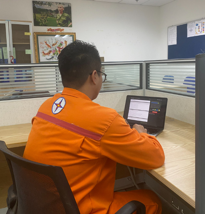 A person in an orange uniform sitting at a desk using a computer  Description automatically generated