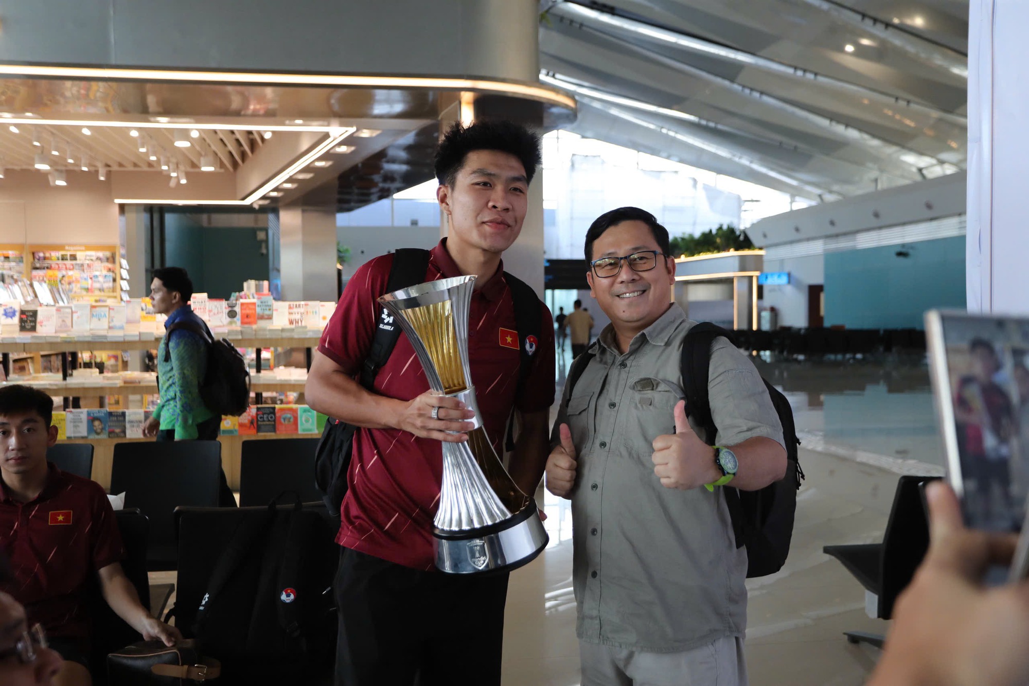 Dinh Bac “តស៊ូ” ដើម្បីដណ្ដើមពានរង្វាន់ អ្នកគាំទ្រឥណ្ឌូណេស៊ីបានសុំប័ណ្ណសម្គាល់ U.23 វៀតណាមនៅព្រលានយន្តហោះ - រូបថត ២. Đình Bắc ‘khệ nệ’ cầm cúp, CĐV Indonesia xin chữ ký U.23 Việt Nam ở sân bay- Ảnh 2.