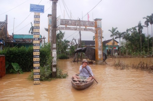 Người dân dùng thuyền đi lại cạnh cột mốc báo lũ