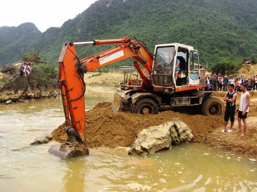 Máy múc đổ đất, tiến ra giữa dòng để kéo gỗ
