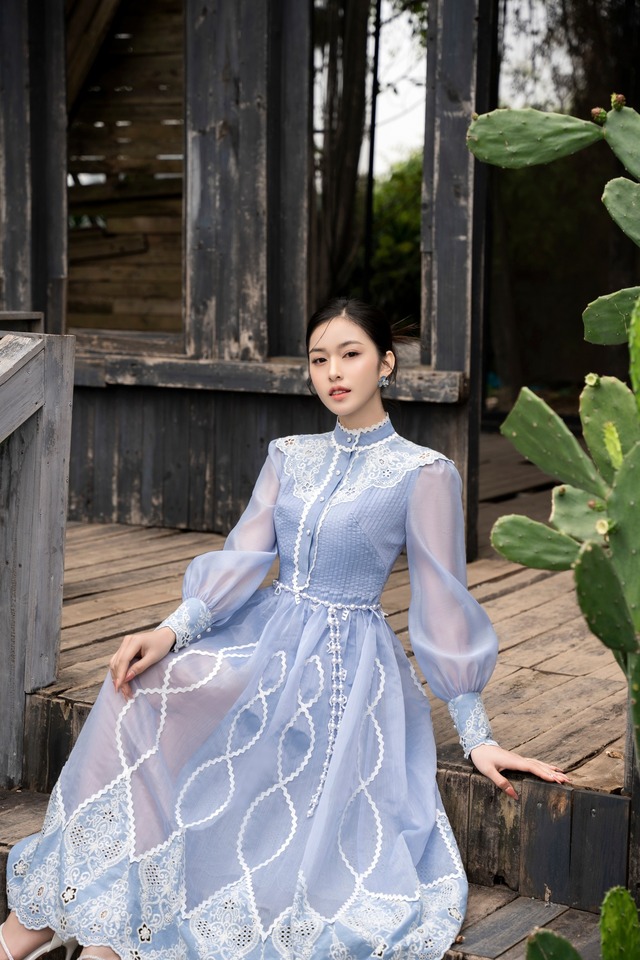 Chất vải organza phối ren đục lỗ và đăng ten viền tạo họa tiết sống động cho thiết kế cổ trụ tay chít phồng duyên dáng màu xanh nhạt. Kỹ thuật xếp ly nhuyễn được khéo léo bố trí ở phần thân trên tạo hiệu ứng vòng 2 thon gọn và quyến rũ hơn