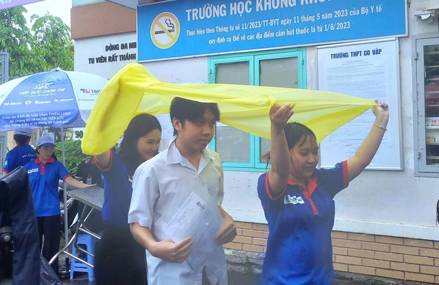 Tình nguyện viên chấp nhận ướt người để giữ khô giấy tờ cho thí sinh - Ảnh 1.