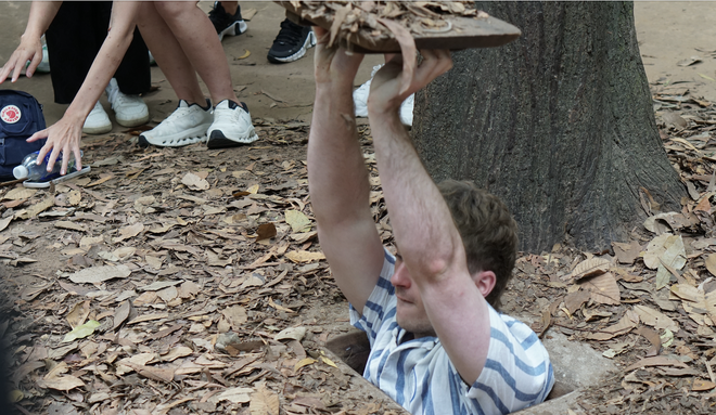 Västerländska turister lyssnar uppmärksamt på guiden som berättar historier vid Cu Chi-tunnlarna - Foto 3.