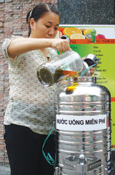 Chủ nhân bình trà từ thiện trên đường Điện Biên Phủ (P.Đa Kao, Q.1) thêm trà đá vào bình để “tiếp sức” cho người đi đường - Ảnh: Bùi Chiến