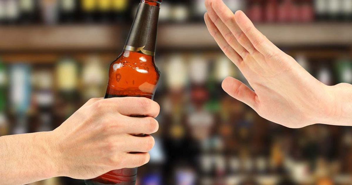 Một tay đưa chai bia, tay kia giơ lên từ chối, nền phía sau là quầy bar mờ.
