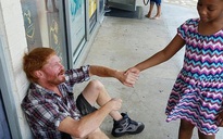 Bé gái da màu nắm tay an ủi người vô gia cư da trắng