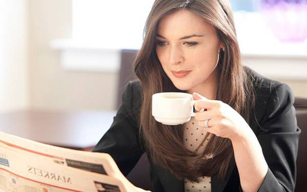 Người phụ nữ đang mỉm cười và thưởng thức một ly cà phê ngon trong một quán sang trọng.